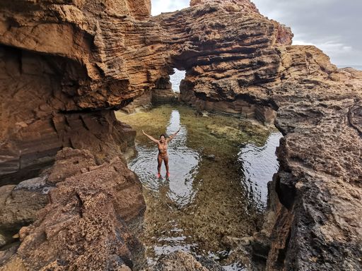 A woman in a bikini raises her arms happily enjoying the adventure of finding caves at the sea edge