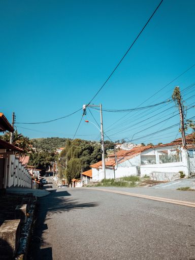 A vertical shot of an asphalt road amid residential buildings under a blue sky - electric lines