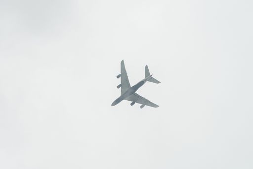 A low angle shot of an airplane soars through the sky, against a backdrop of white fluffy clouds
