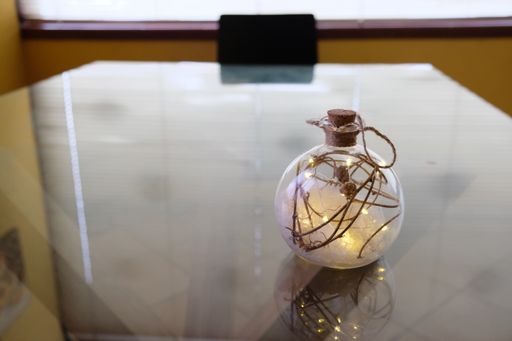 A closeup of a transparent Xmas ball with illuminated golden lights isolated on a reflective table