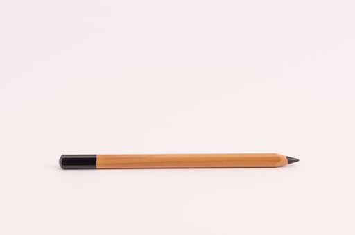 A closeup of a wooden black pencil on light pink empty surface