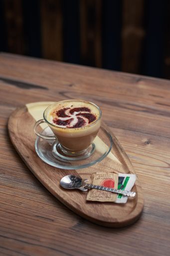 A white plate with a cup of coffee and small portion of food sitting on a wooden table