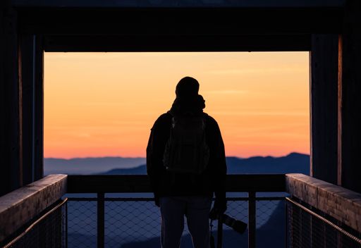 A man standing in an elevated position, gazing out over a mountainous landscape at sunset