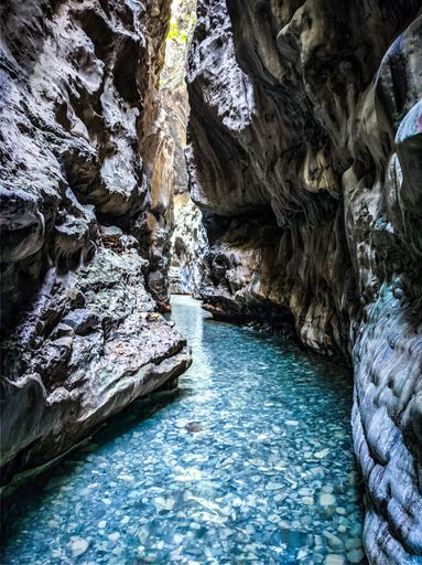 A vertical shot of a narrow river surrounded by tall magnificent rocky cliffs