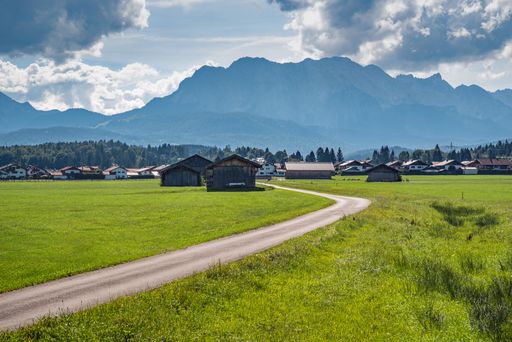 A scenic Alpine landscape with a green field and rural houses in the distance. Upper Bavaria, Germany