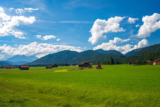 A scenic Alpine landscape with a green field and rural houses in the distance. Upper Bavaria, Germany