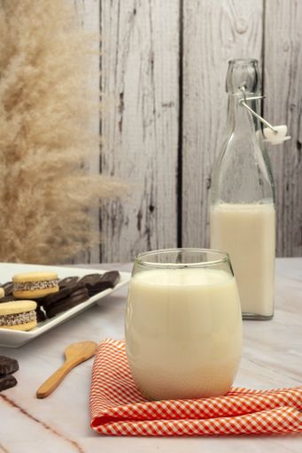 A vertical shot of milk in a glass and in bottle and cookies on a white plate