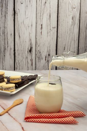 A vertical shot of a glass filled with milk from a bottle and cookies in the background