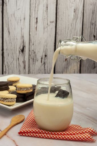 A vertical shot of a glass filled with milk from a bottle and cookies in the background