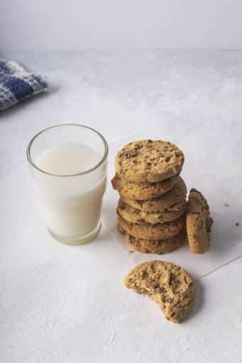 A stack of peanut butter cookies by a glass of fresh milk on a white table