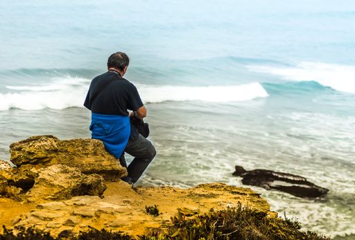 A closeup of a male sitting on coastal rock while enjoying the seascape