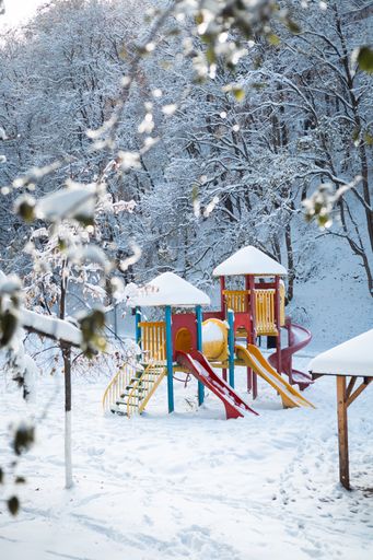A winter scene of a snow-covered children's playground situated in a wooded area