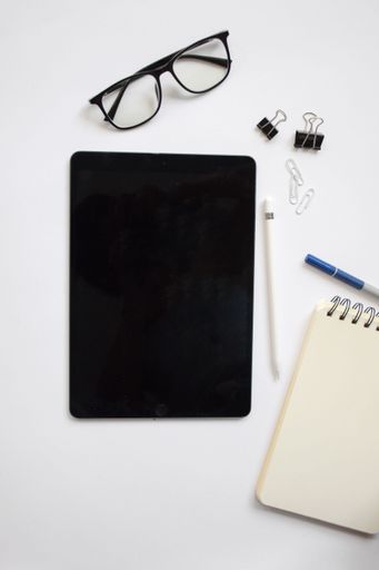 A top view of a tablet with a black screen with stationery on a white table