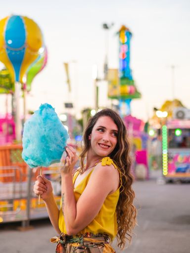A vertical shot of an attractive Caucasian female posing with blue cotton candy at a carnival
