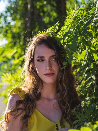 A beautiful caucasian girl posing near the leaves of the tree in the sun during summer