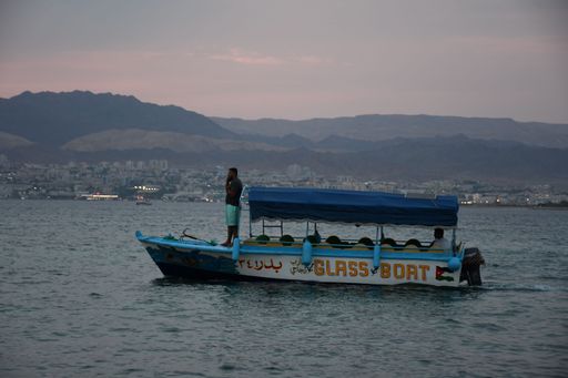 A boat floating on the Jordanian side of the Red Sea with a view of Eilat in the background
