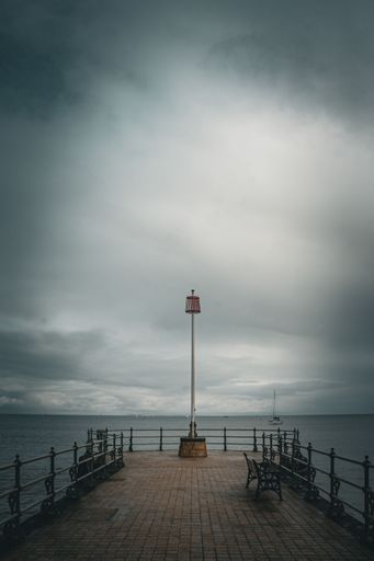 A lamp post on a pier against the sea on a cloudy day