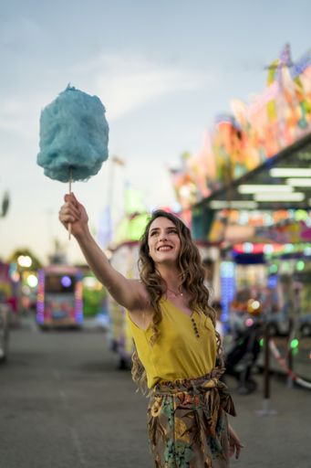 An attractive young female standing with cotton candy in hand and spending time in an amusement park