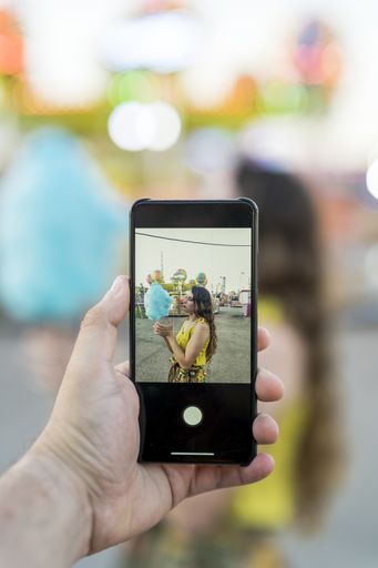 A vertical shot of a male taking a picture on his smartphone of a female holding cotton candy