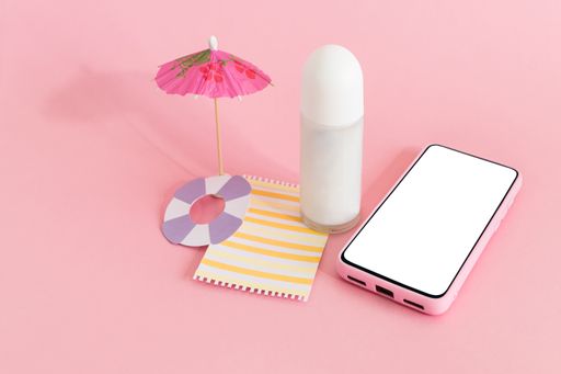 The skincare cream bottle container with small beach umbrella and smart phone on pink background