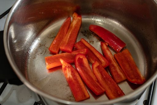 A high angle shot of red bell pepper pieces in a steel bowl on stove