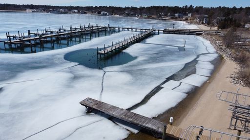 An aerial view of a tranquil winter scene featuring a lake partially covered in ice in Beaver Island, Michigan