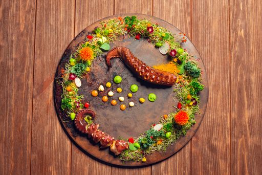 A top view of Octopus tentacles with edible flower decoration on a wooden table