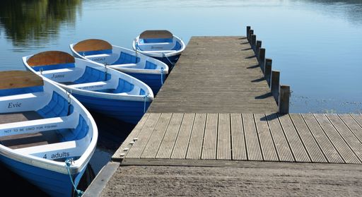 Four rowing boats with individual names tied to a jetty on Llangorse Lake in South Wales.