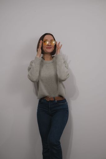 A young female adult is standing with her hands covering her face, looking down in a contemplative gesture