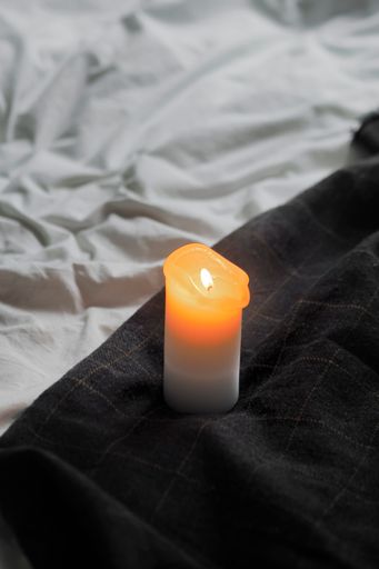 A white candle lit on a black linen-covered bed, creating a peaceful and serene atmosphere