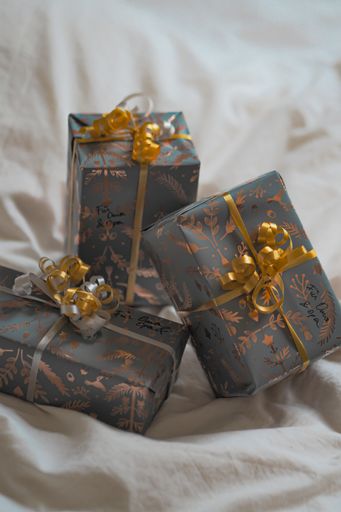Four wrapped gift boxes resting on a bed with gold bows and ribbons adorning each