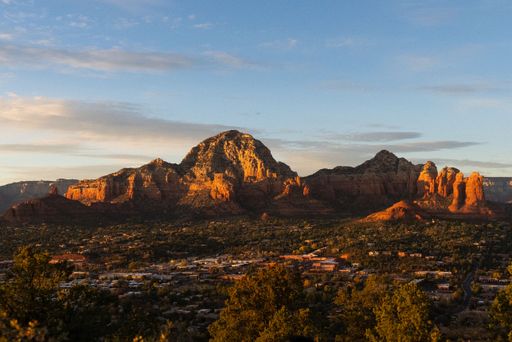 A breathtaking landscape of red and green hues featuring rocky outcrops and pine trees against the backdrop of a golden sunset