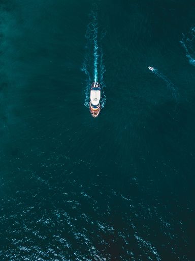 This image depicts a small wooden boat floating in a tranquil body of water on a bright, sunny day with a beautiful blue sky in the background