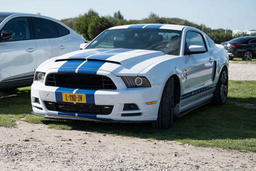An out of focus photo of a typical fifth generation Ford Mustang American sports car, white with Shelby blue stripes