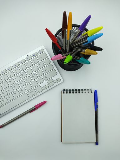An overhead shot of an office desk with colorful pens and a keyboard