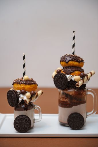 A vertical shot of chocolate milkshakes with donut and cookie decorations