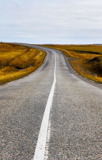 A scenic country road stretches across the horizon of a vast, open field. Iceland