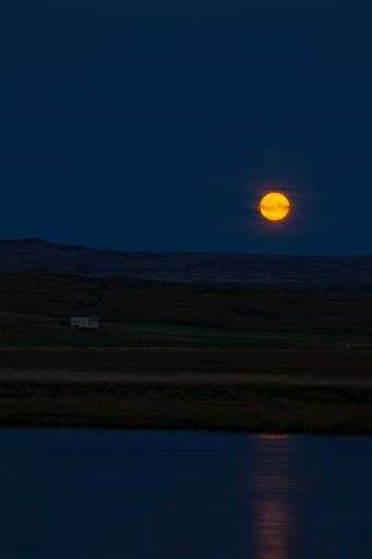 A tranquil night sky illuminated by a bright full moon above a rural landscape. Iceland