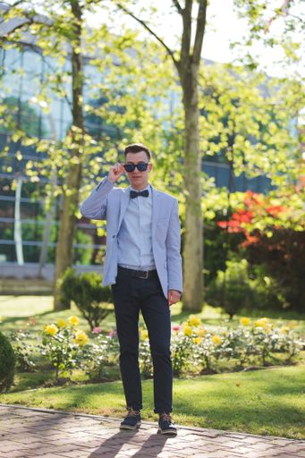 A young handsome elegant man in a suit with a bow and sunglasses posing in the park