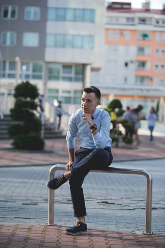 A young Caucasian male in a formal outfit sitting and waiting on a street