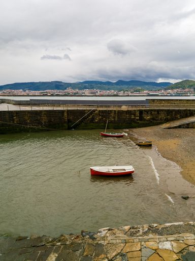 A vertical shot of boats by the water with a coastal city in the background