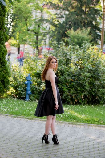 A vertical shot of a white Caucasian woman wearing a classy black dress and posing for a picture