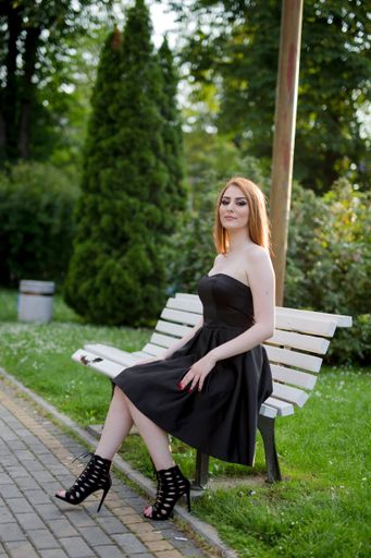 A vertical shot of a young Caucasian lady in an elegant dress and look sitting on a bench