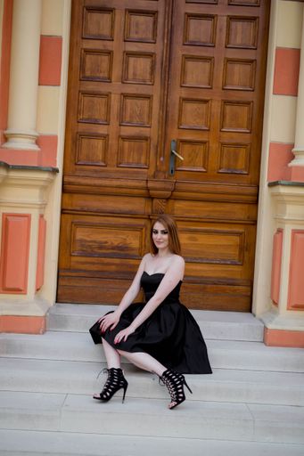 A vertical shot of a white Caucasian woman wearing a classy black dress and posing for a picture