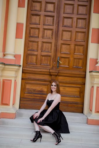 A vertical shot of a young blonde female posing in an elegant black strapless dress