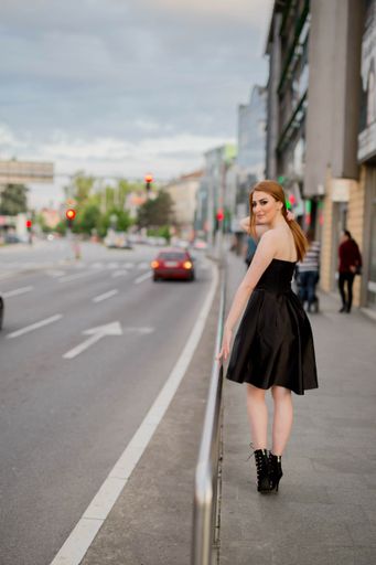 A young Caucasian female with beautiful makeup wearing an elegant black dress walking on a street