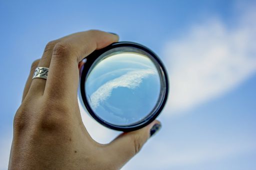 A female hand holding a magnifying glass on cloudy sk