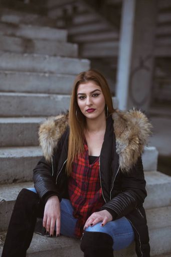 A vertical shot of a beautiful Bosnian Caucasian woman wearing a jacket and jeans, sitting on the stairs outdoors