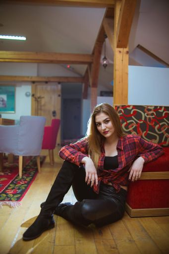 A vertical shot of a young woman sitting on a room floor and leaning on a couch