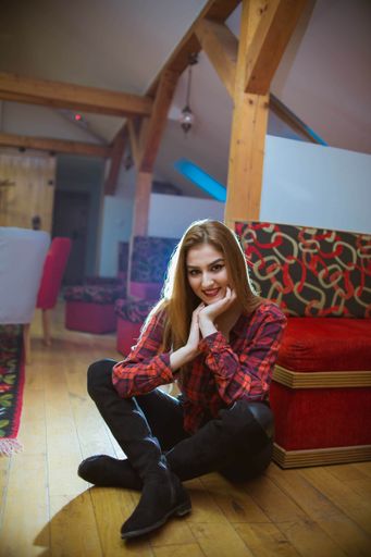 A vertical shot of a beautiful Bosnian Caucasian woman wearing a shirt and leather pants, sitting indoors